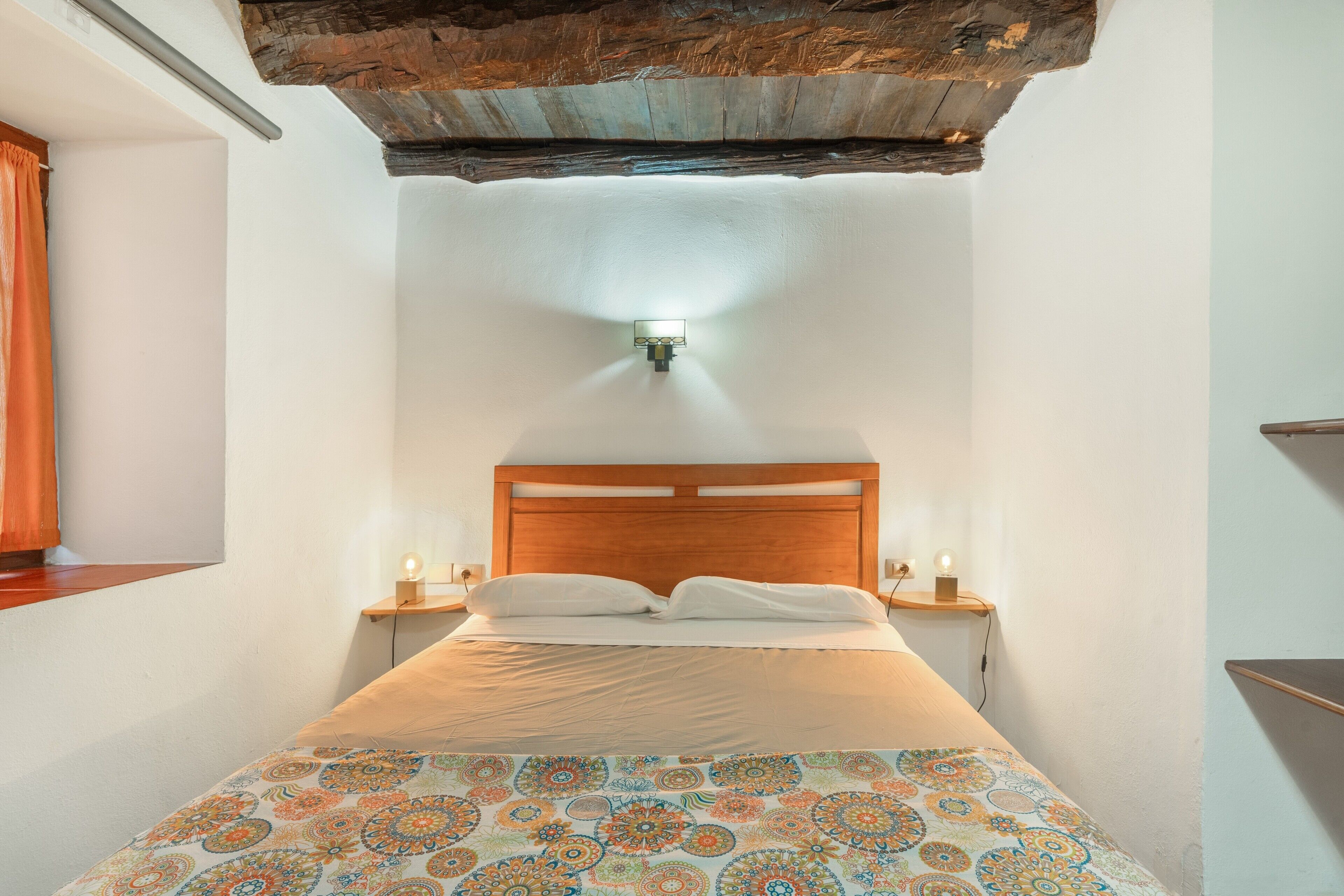 Een slaapkamer met een houten hoofdbord, een bed met een dessin, twee bedlampen en een wandlamp.