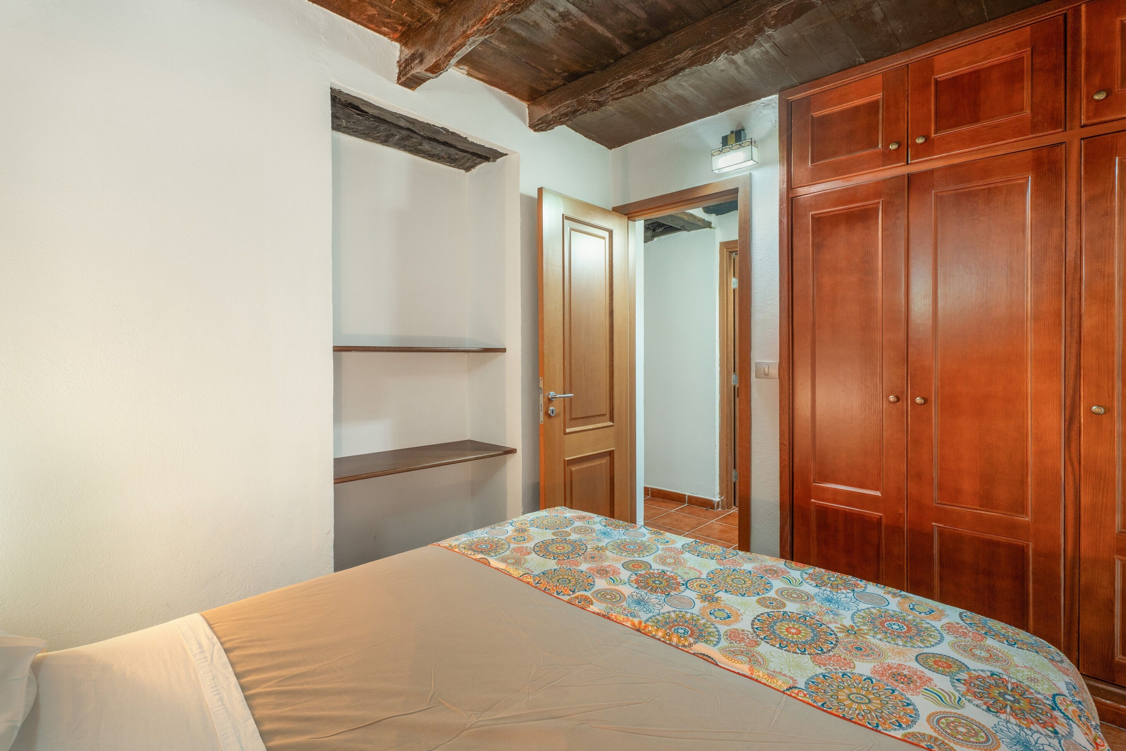 Un dormitorio con cama, armario de madera y puerta que da a otra habitación.