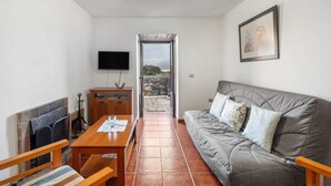 A living room with a sofa, a wooden table, a TV, and a fireplace. - Apartment El Peral in 'Casa Rural Los Perales' with Sea Views, Shared Terrace and Wi-Fi (Mocanal)