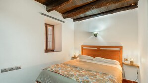 A bedroom with a wooden headboard, a patterned bedspread, a small window, and a nightstand with a lamp. - Apartment El Peral in 'Casa Rural Los Perales' with Sea Views, Shared Terrace and Wi-Fi (Mocanal)