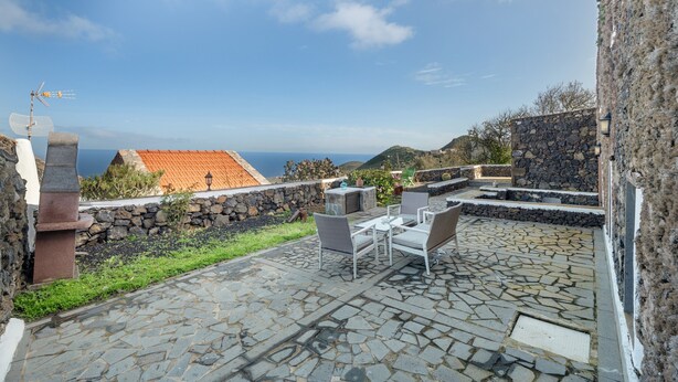A stone patio with outdoor furniture, a stone wall, and a view of the sea. - Apartment El Peral in 'Casa Rural Los Perales' with Sea Views, Shared Terrace and Wi-Fi (Mocanal)