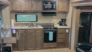 Una cocina compacta con armarios de madera, microondas, estufa y refrigerador.