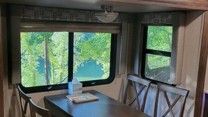 Un comedor con una mesa y sillas, una ventana con vista a follaje, y una lámpara en el techo.