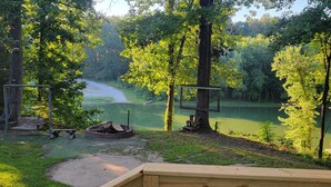 Un camping con un pozo de fuego, un conjunto de columpios y vistas a un lago rodeado de árboles.