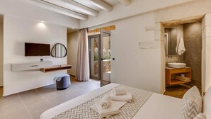 Una habitación de hotel moderna con una cama, televisor, baño con lavamanos y espejo, y vistas al exterior.