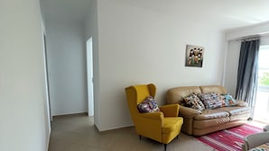 A living room with a yellow armchair, a beige sofa, and a dining table with a colorful table runner.