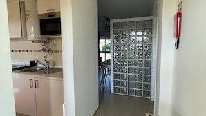 A kitchen with white cabinets, a microwave, and a water heater. There is a red rug in the foreground and a door with a glass panel in the background.