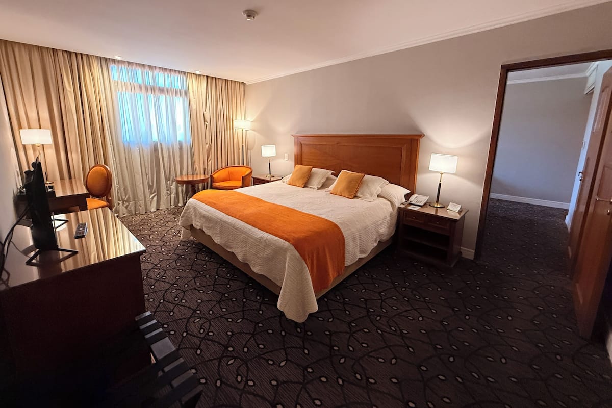 Een hotelkamer met een groot bed, een bureau met stoel, een klein tafeltje en een lamp.