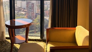 Une chambre d’hôtel avec un canapé, une petite table ronde et une grande fenêtre donnant sur la ville.