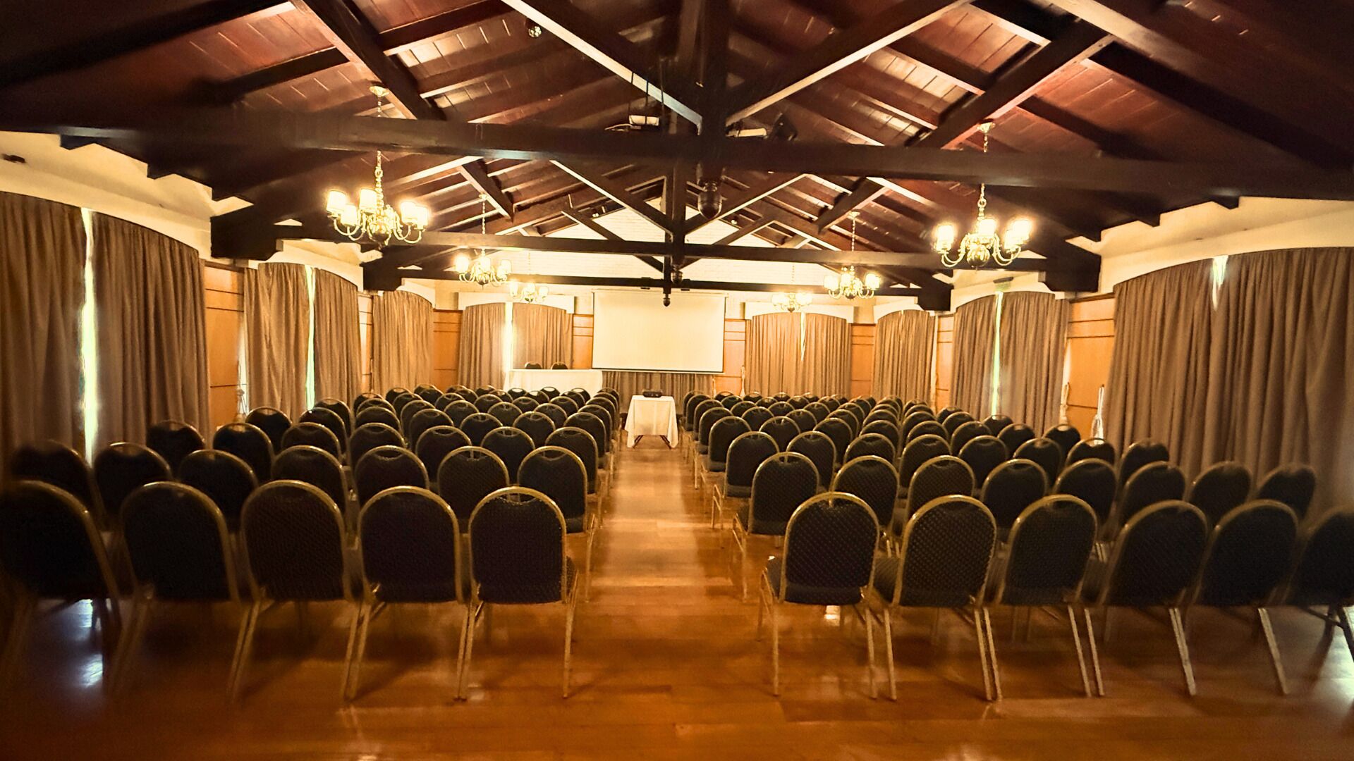 A conference room with rows of chairs, a large screen, and chandeliers.