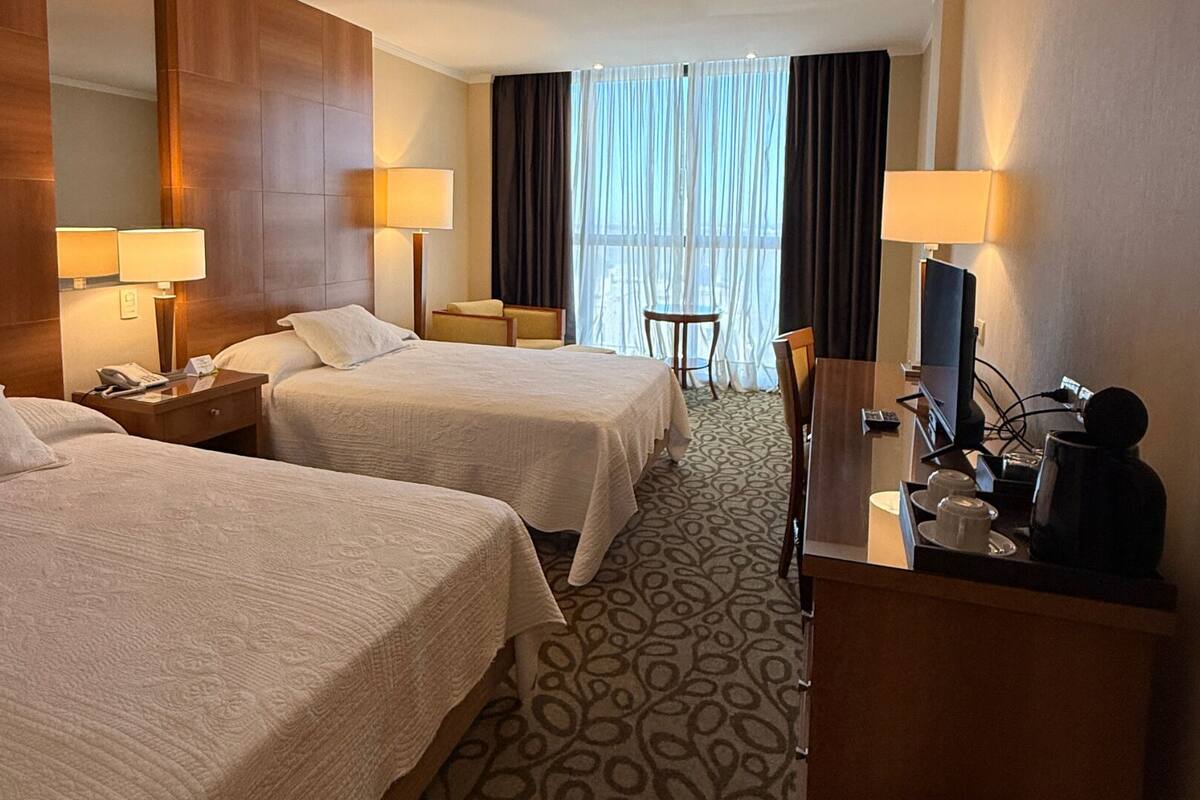 Een hotelkamer met twee bedden, een bureau met een computer, een televisie en een klein tafeltje.