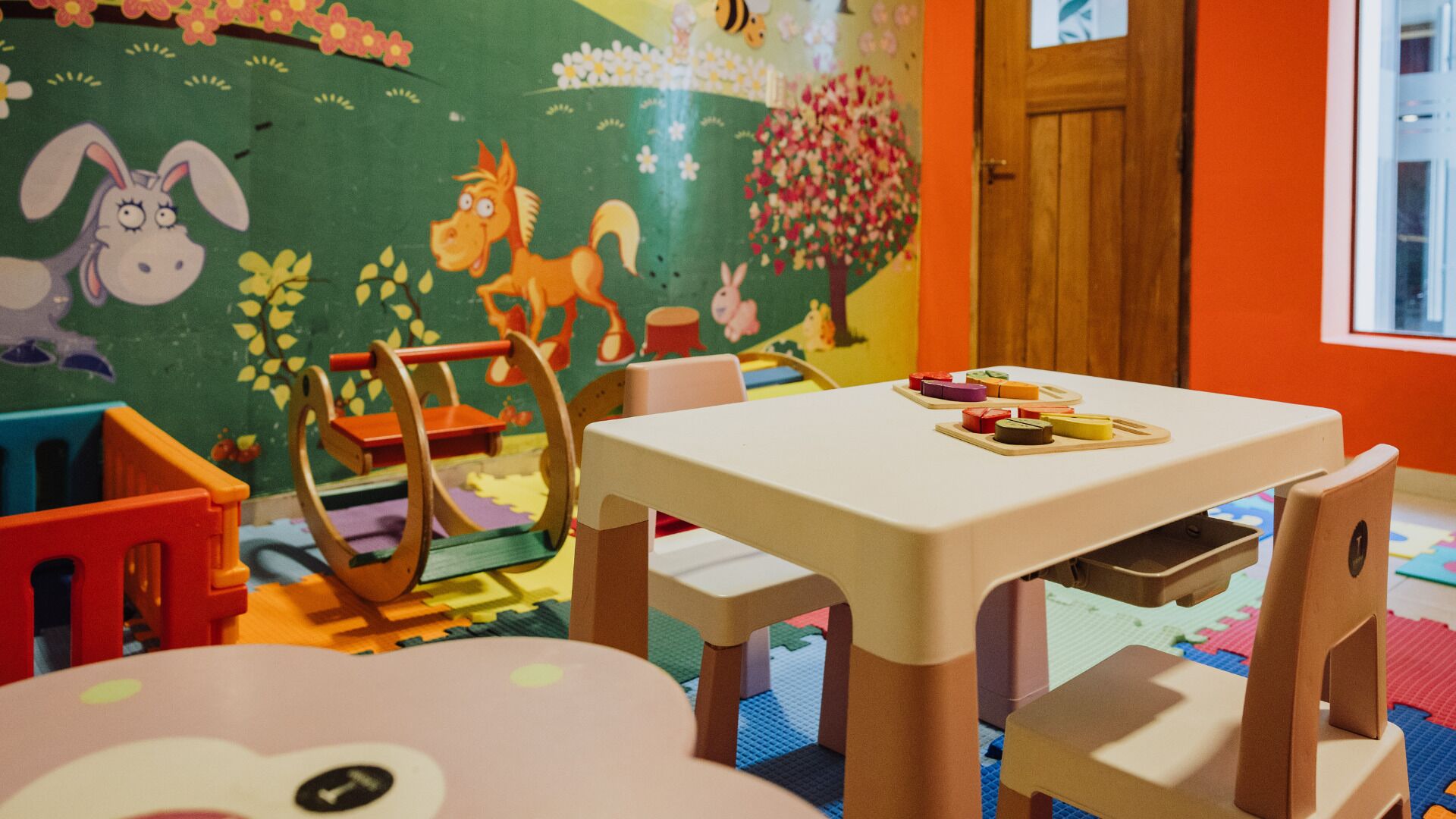 A children's playroom with colorful toys, a table, chairs, and a mural on the wall.