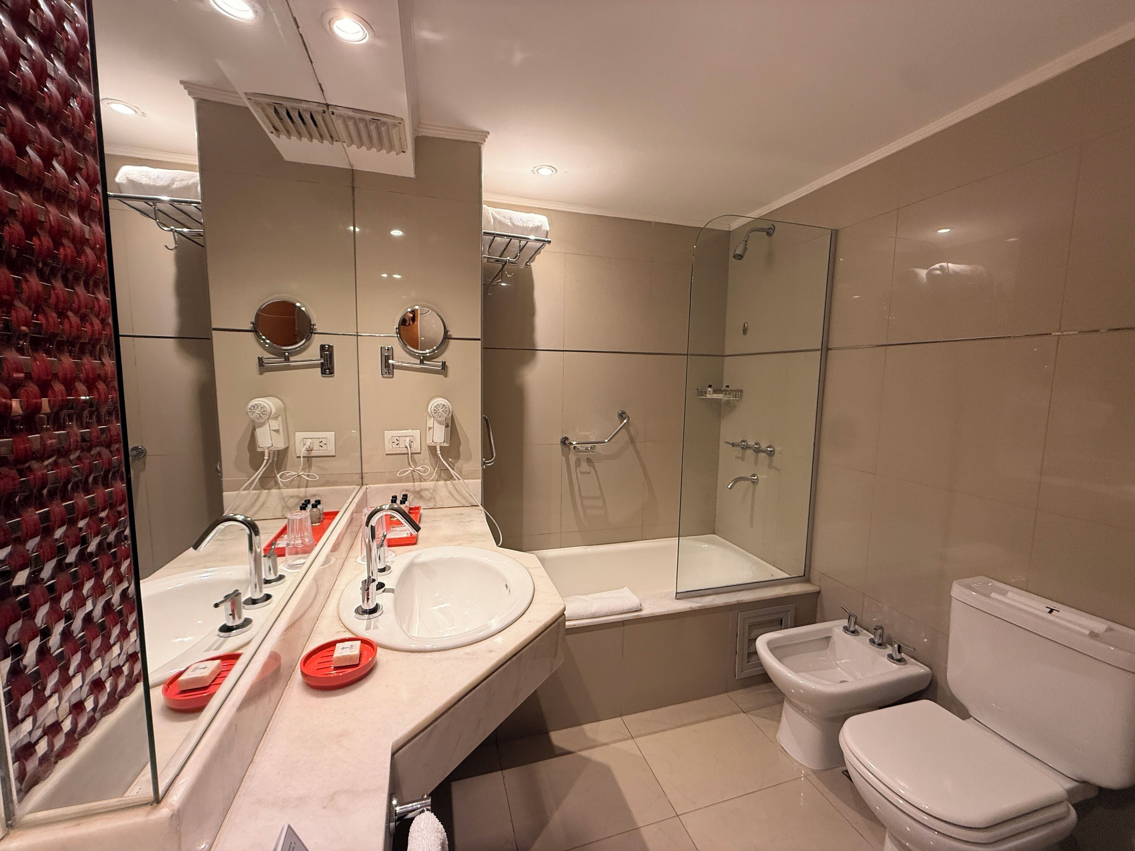 A modern bathroom with a large mirror, a bathtub, a shower, and a toilet.