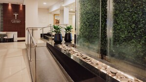 Een hotel lobby met een receptiebalie, een trap, potplanten en een waterval.
