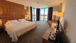Een hotelkamer met een groot bed, een bureau met een computer, een stoel en uitzicht op de omgeving.