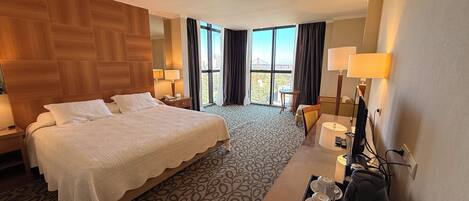 A hotel room with a large bed, a desk with a computer, a chair, and a view of the outdoors.