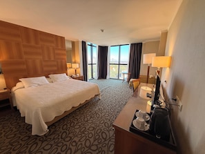 Une chambre d’hôtel avec un grand lit, un bureau équipé d’un ordinateur, une chaise et une vue sur l’extérieur.