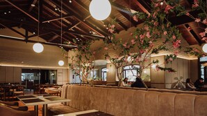 Een restaurant met hoge plafonds, zichtbare balken en hangende吊灯. Er zijn houten tafels en zitplaatsen met kussens.