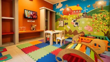 A children's playroom with a colorful mural, a television, a play table, and a playpen.