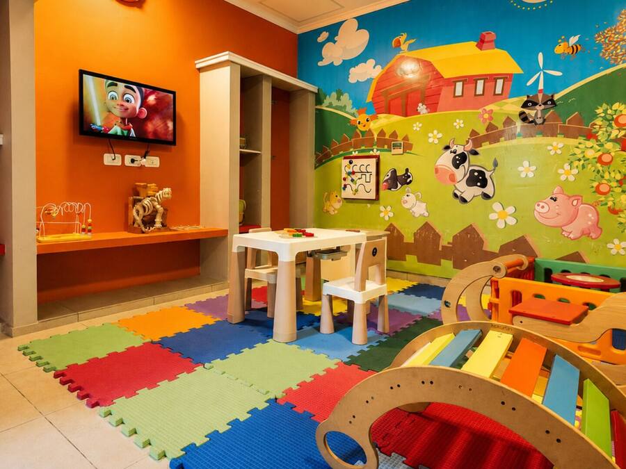 A children's playroom with a colorful mural, a television, a play table, and a playpen.