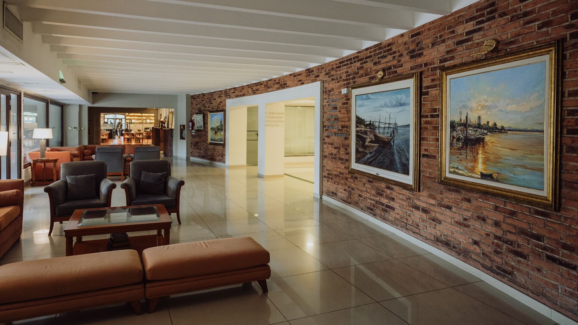 Un vestíbulo con pared de ladrillo, una zona de estar con sillones y sofá de cuero, y dos cuadros enmarcados.
