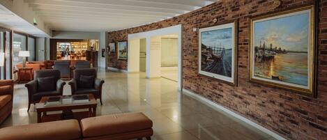 A lobby with a brick wall, a seating area with leather chairs and a sofa, and two framed paintings.