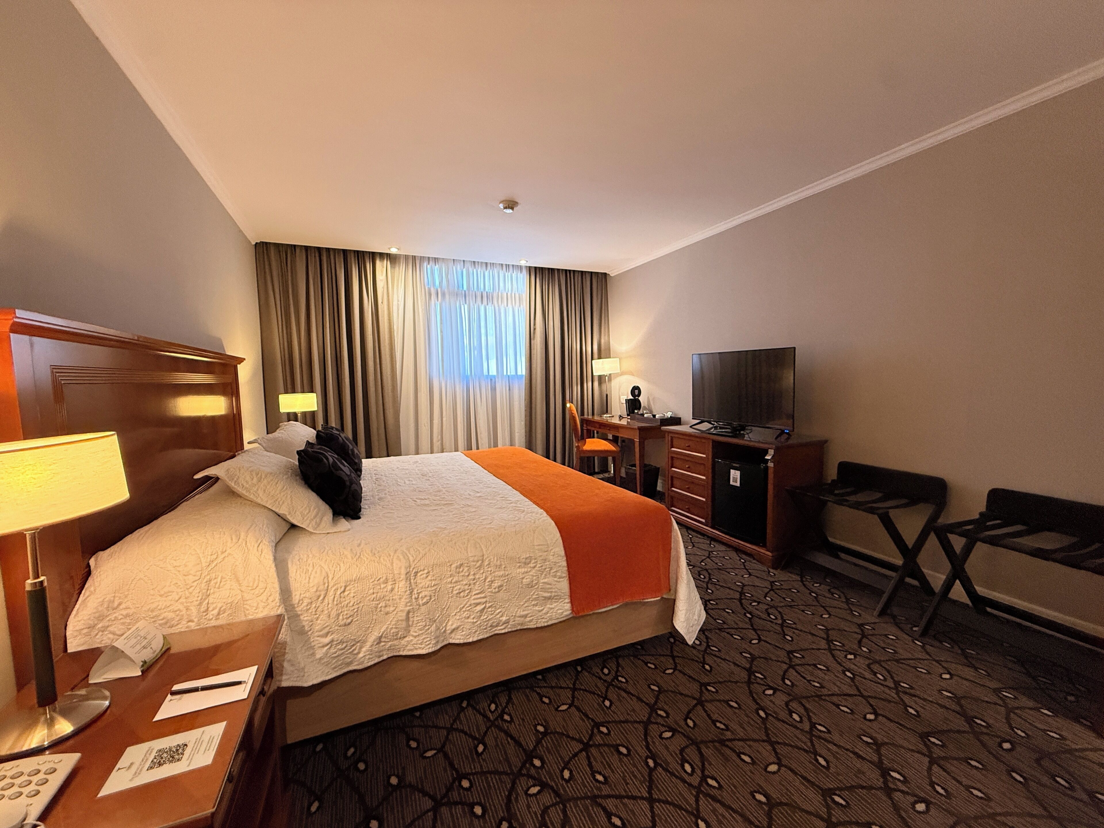 Een hotelkamer met een bed, bureau, stoel, televisie en een kamerbreed tapijt met dessin.
