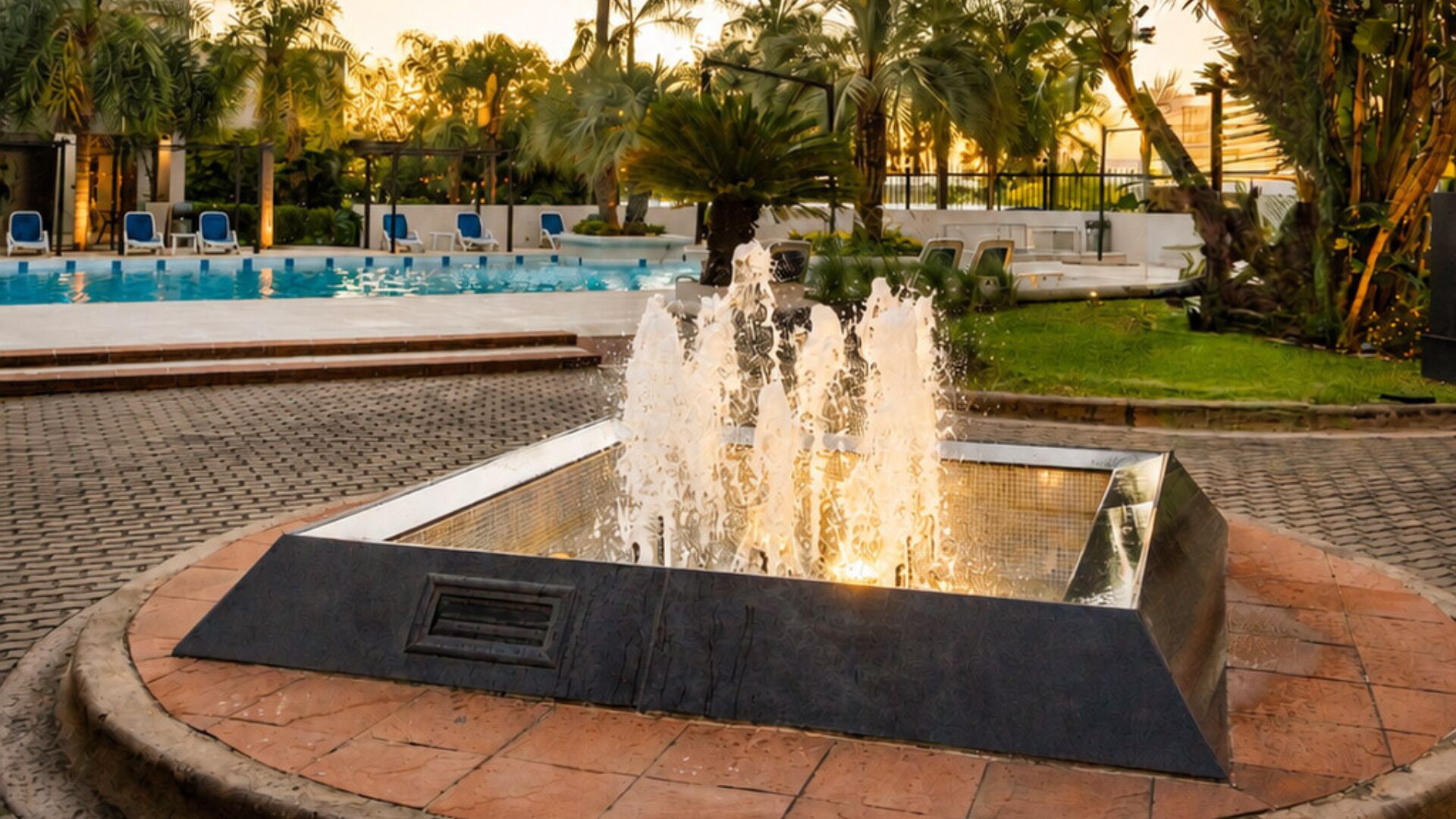 Ein Schwimmbecken mit Springbrunnen, umgeben von Liegestühlen und Palmen.