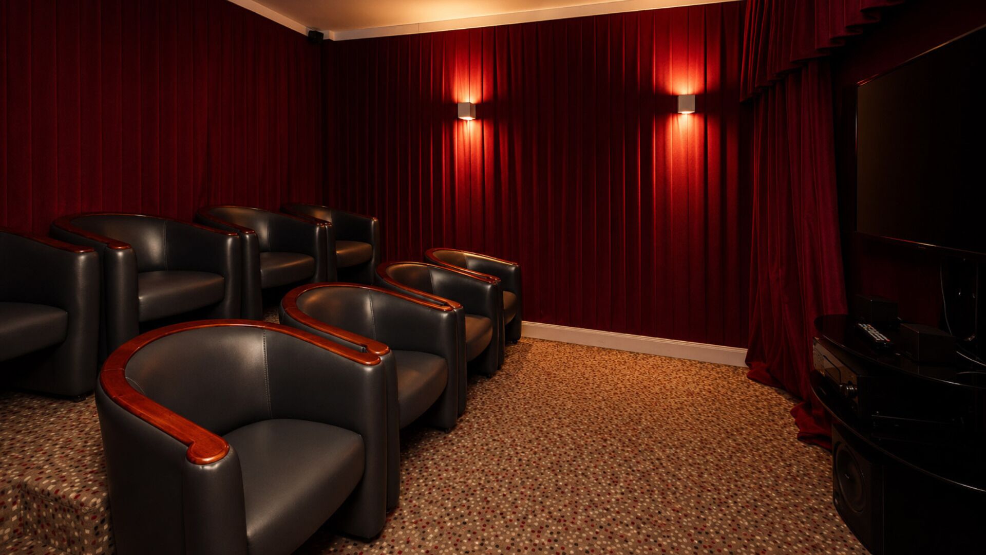 Une salle de théâtre avec des rideaux rouges, des fauteuils en cuir noir et un écran.