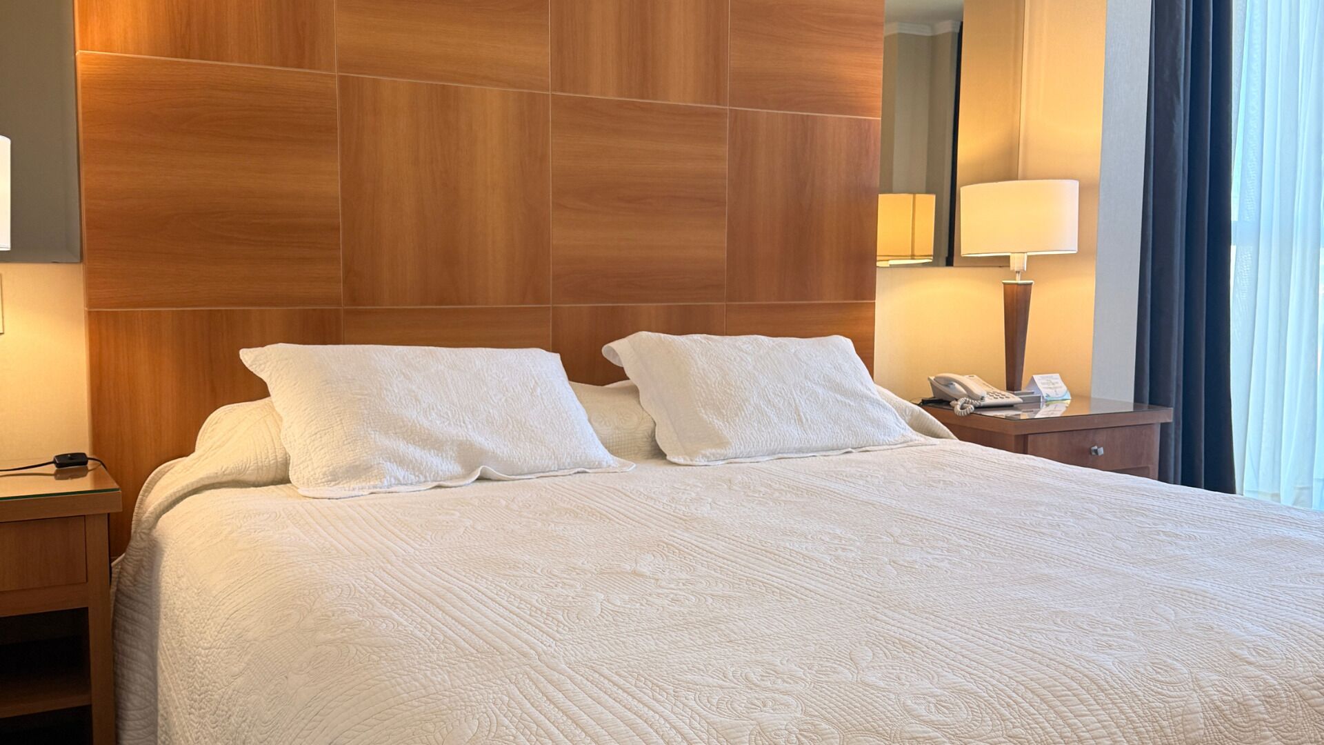 A hotel room with a large bed, two pillows, a nightstand with a lamp, and a phone.