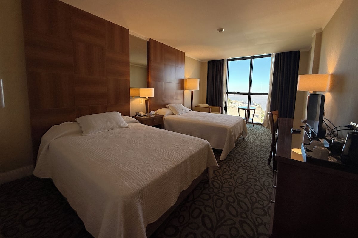 Hotelkamer met twee bedden, een bureau, een stoel, een televisie en een groot raam met uitzicht.