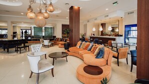 Un hall de hotel con un piano, sofás, sillones, una zona de bar y un espejo grande.