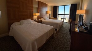 Een hotelkamer met twee bedden, een bureau met een computer en een groot raam met uitzicht.