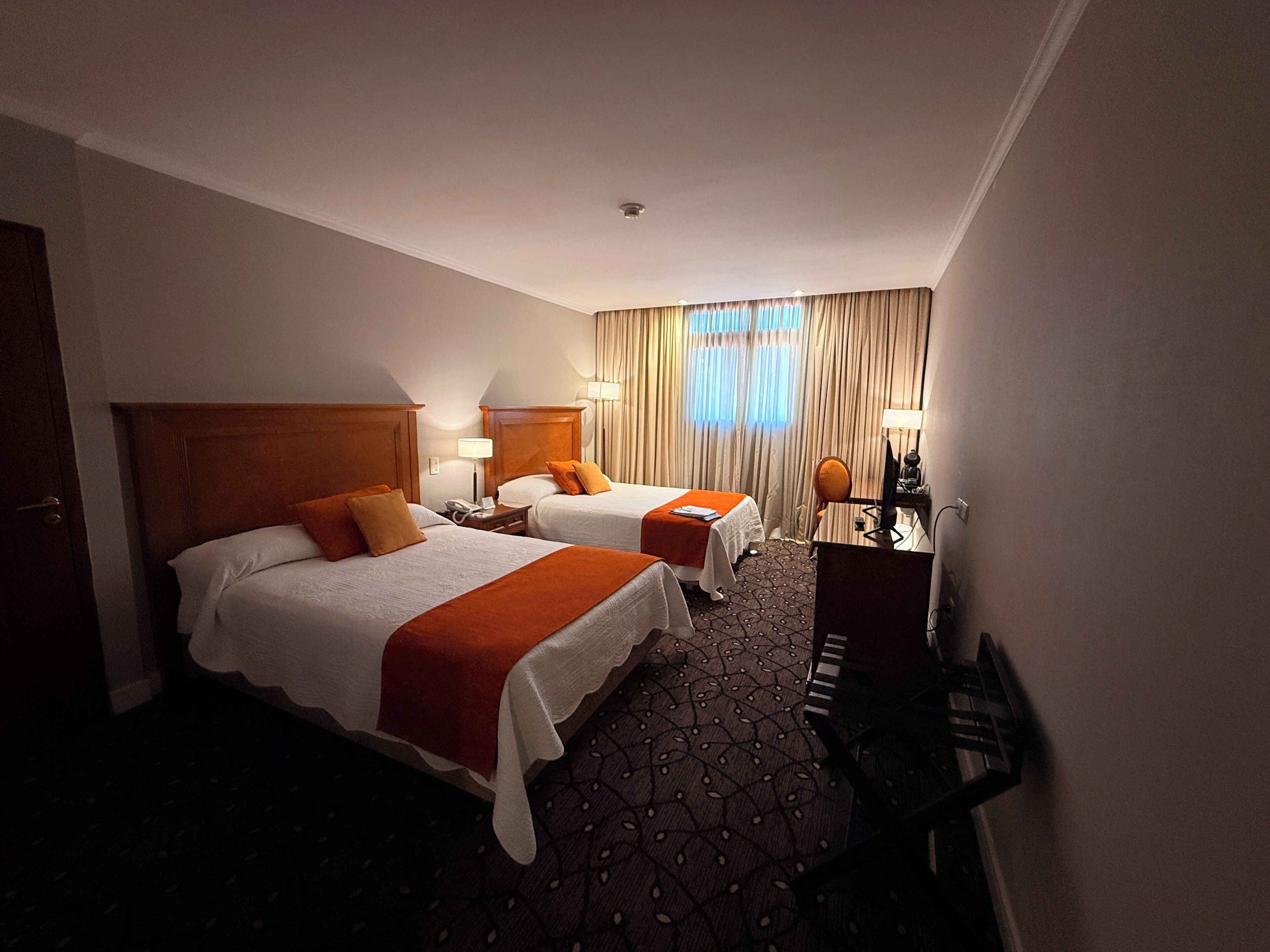Habitación de hotel con dos camas, un escritorio, una silla, un televisor y una ventana con cortinas.
