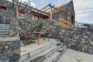 A stone building with a wooden pergola, a table with chairs, and a staircase leading to a door. - Country House 'El Moral' with Sea View, Shared Terrace and Wi-Fi (Valverde)