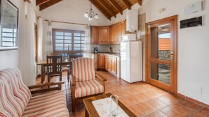 Amplia sala de estar con techo de madera, una mesa de comedor, un sofá a rayas y una cocina con armarios de madera y un refrigerador.