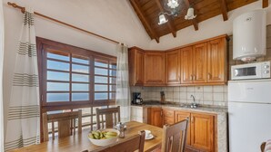 Una cocina con armarios de madera, una mesa de comedor con sillas, una ventana con cortinas y un microondas.