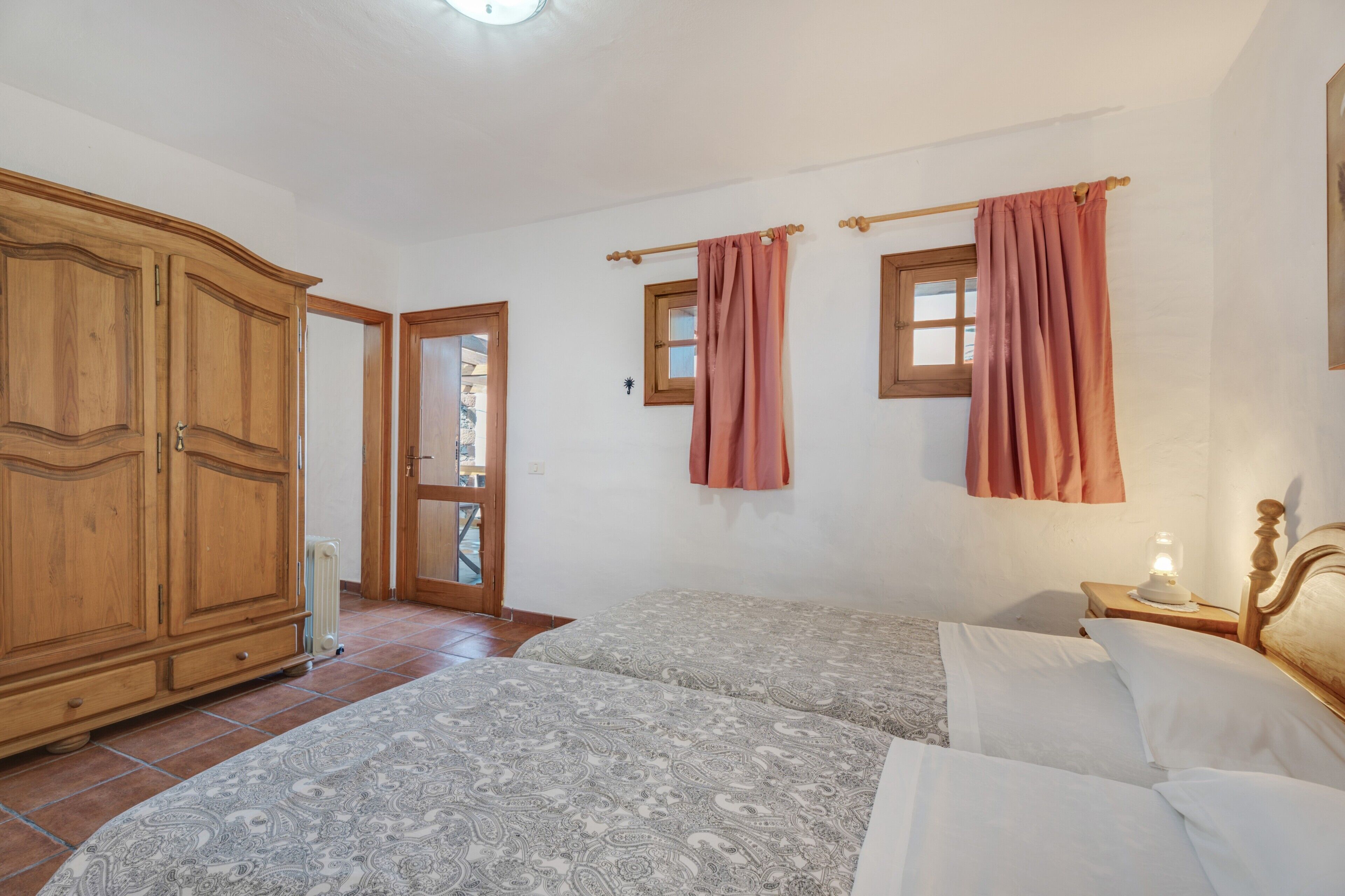 A bedroom with two beds, a wardrobe, a radiator, and a window with curtains.