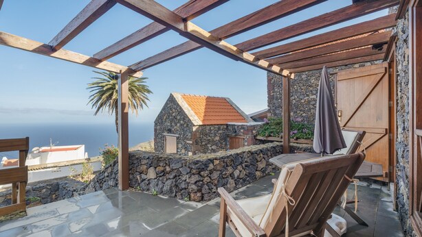 Un espacio al aire libre cubierto con paredes de piedra, una pérgola de madera y vistas al mar.