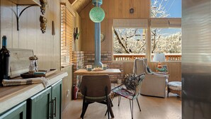 A cozy kitchen with wooden cabinets, a hanging light fixture, and a view of trees outside. - Views•Fully Fenced•BBQ•Spacious Deck•Relaxing Retreat (Lake Arrowhead)