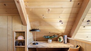 A cozy wooden room with a slanted ceiling, a desk with a lamp, a plant, and books. - Views•Fully Fenced•BBQ•Spacious Deck•Relaxing Retreat (Lake Arrowhead)