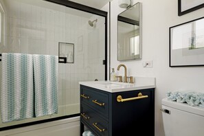 A bathroom with a glass shower enclosure, a white sink with a gold faucet, and a black vanity with gold handles. - MCM Vintage Fireplace•Views•Fully Fenced•BBQ•Large Deck (Lake Arrowhead)