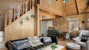 A wooden interior with a staircase, a black leather sofa, a dining area, and a kitchen. - Views•Fully Fenced•BBQ•Spacious Deck•Relaxing Retreat (Lake Arrowhead)