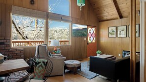A cozy cabin interior with wooden walls, large windows, a dining area, and a living space. - Views•Fully Fenced•BBQ•Spacious Deck•Relaxing Retreat (Lake Arrowhead)