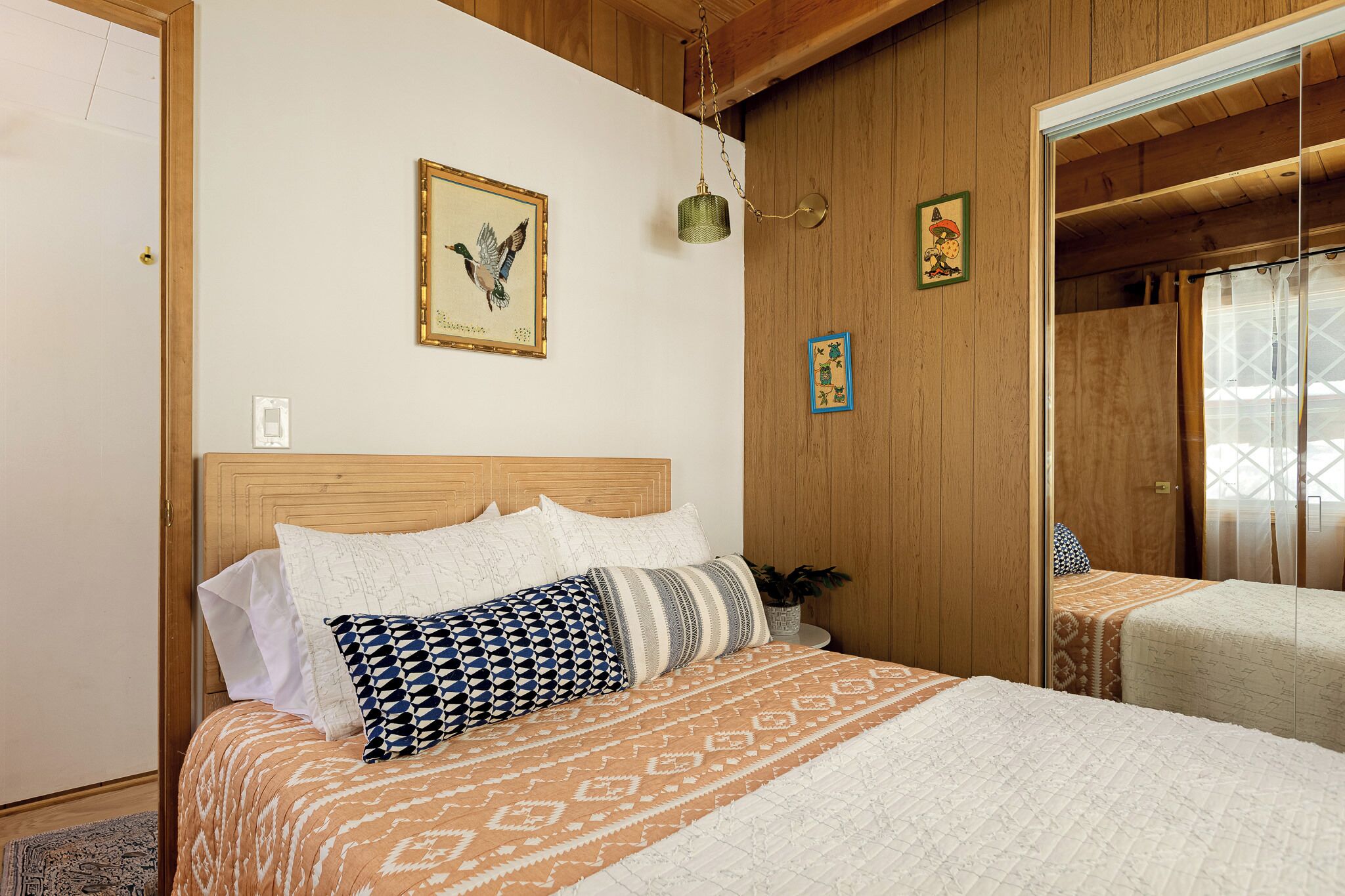 Un dormitorio con cabecera de madera, colcha estampada y una mesita de noche con una planta.