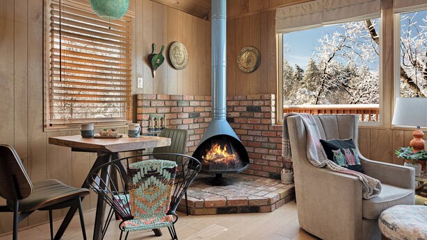 A cozy room with a fireplace, wooden walls, and a view of snow-covered trees. - Views•Fully Fenced•BBQ•Spacious Deck•Relaxing Retreat (Lake Arrowhead)