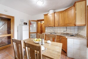 A kitchen with wooden cabinets, a white refrigerator, a microwave, and a dining table with chairs. - Country House 'El Almendro' with Sea Views, Shared Terrace and Wi-Fi (El Mocanal)