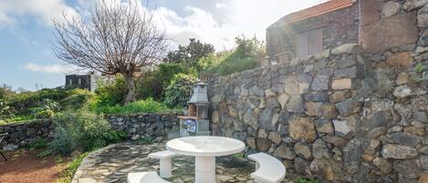 Un mur de pierre agrémenté d’un banc et d’une table en pierre, le tout entouré de verdure et sous un ciel dégagé.