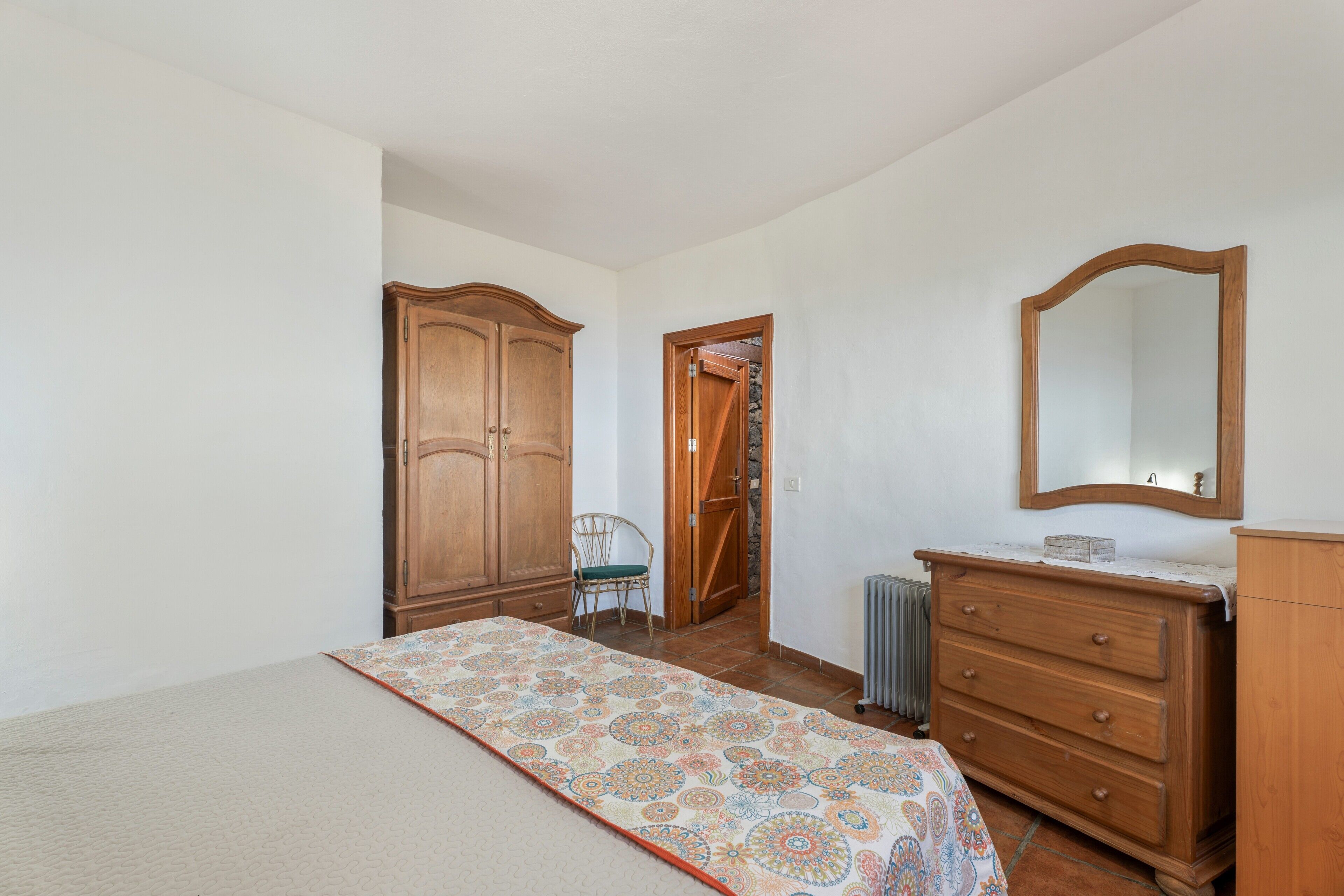 A bedroom with a bed, a dresser, a chair, a wardrobe, and a mirror.