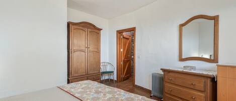 A bedroom with a bed, a dresser, a chair, a wardrobe, and a mirror.